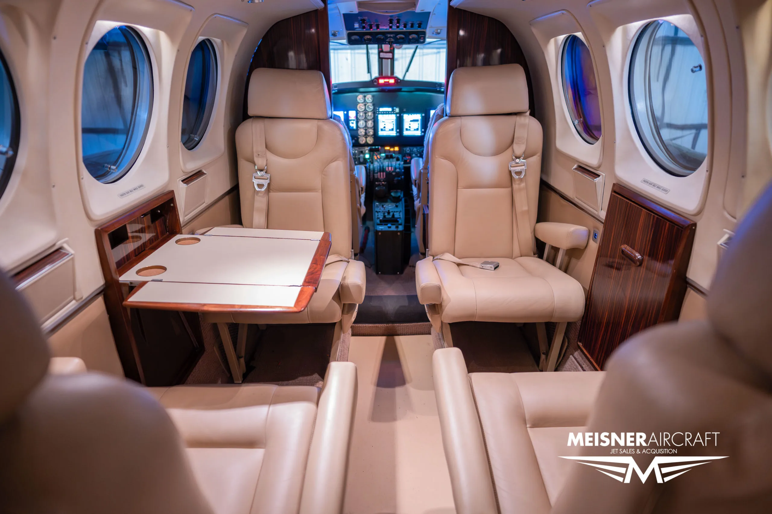 The beige leather interior cabin of a Beechcraft King Air, showing a deployed table and view towards the cockpit.