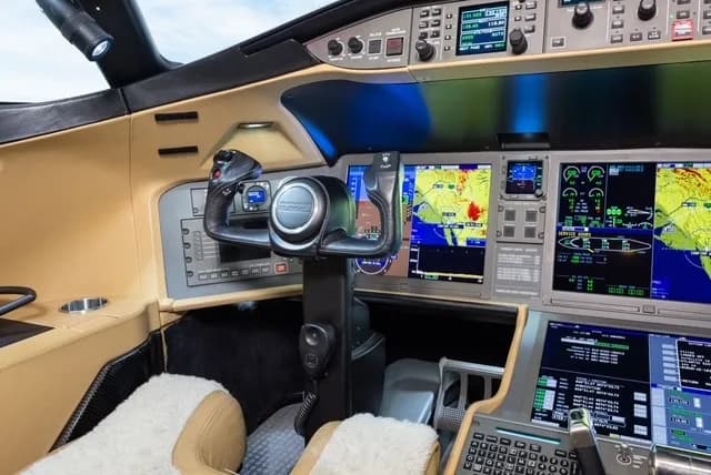 A modern aircraft cockpit with multiple digital displays, a control yoke, and tan interior trim.