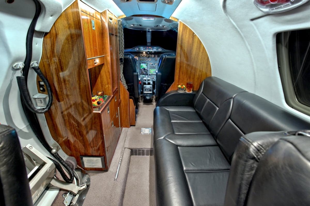 The interior of the Cessna Citation CJ1+ features a leather divan, wood cabinetry, and a view into the cockpit.