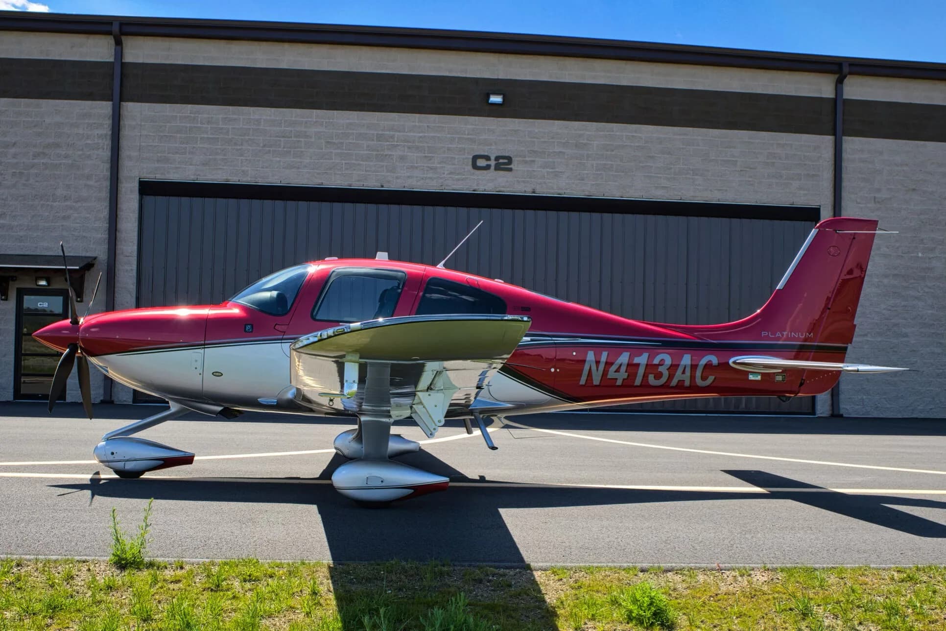 A red and silver Cirrus SR22T aircraft, N413AC, parked next to a hangar on a sunny day.