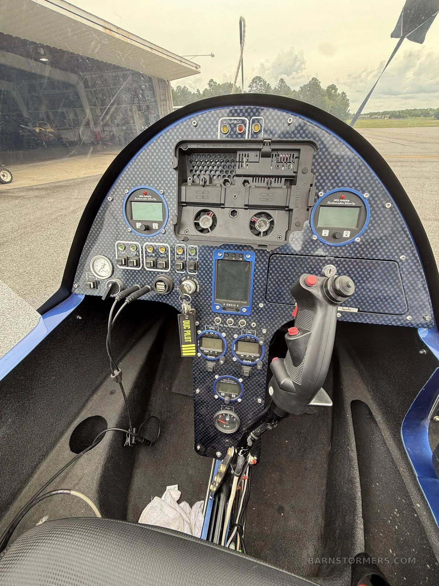 The cockpit of a blue autogyro features a carbon fiber instrument panel with digital displays and a joystick control.