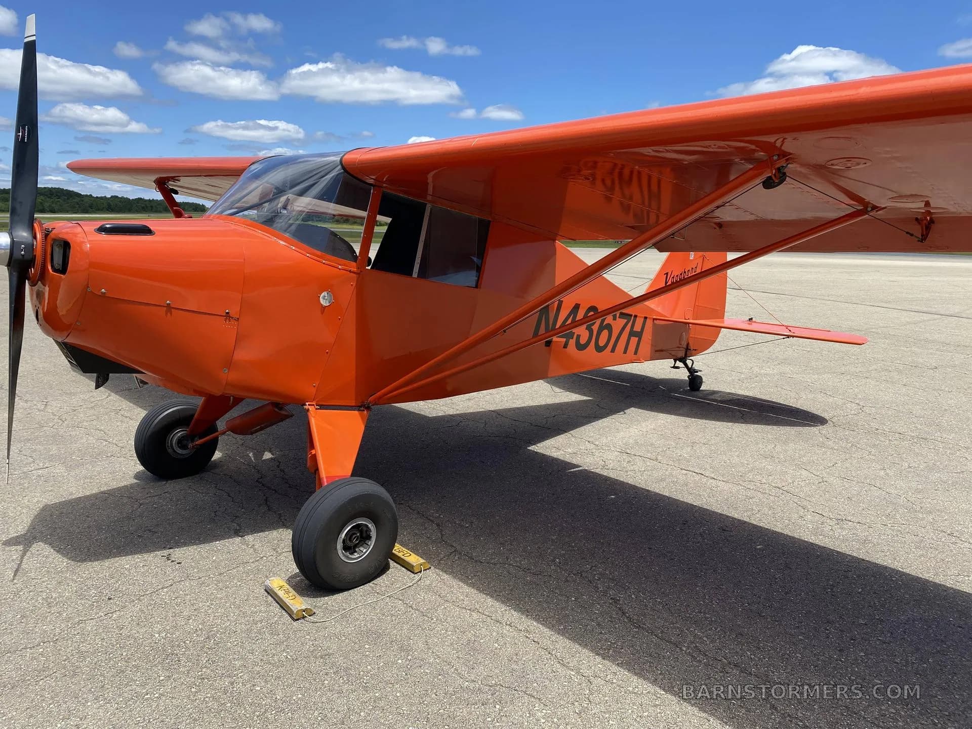 A bright orange single-engine aircraft, registration N4367H, parked on an asphalt runway under a blue sky.