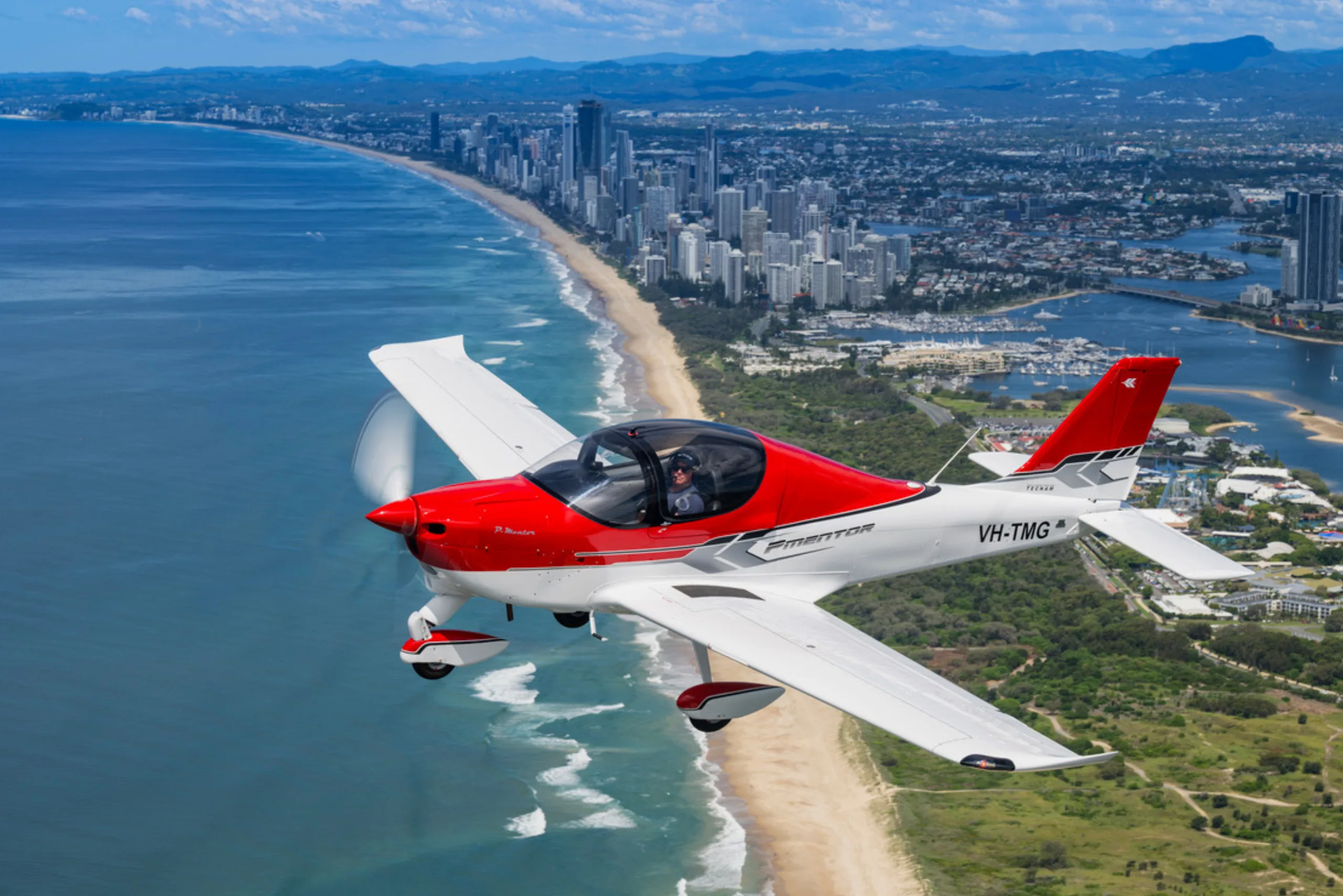 A red and white light aircraft flying over a coastal city.
