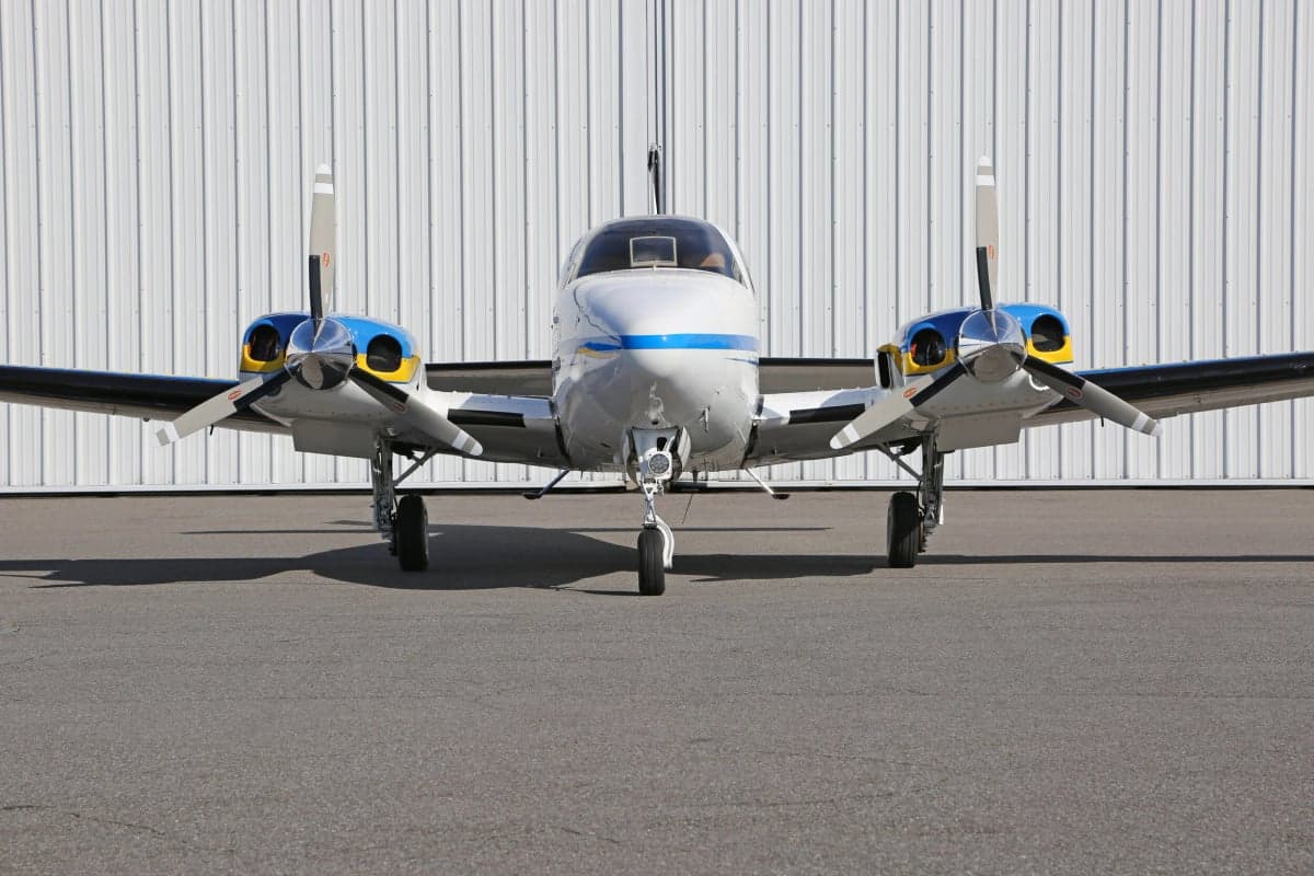Close up front view of a Piper PA-31 Navajo Chieftain aircraft parked on the tarmac in front of a hangar.