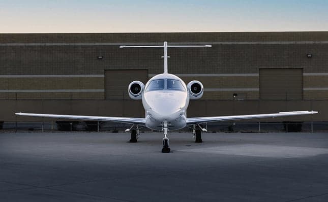 A head-on view of a white business jet with gold and black stripes, tail number N390DP, parked on an airport tarmac.