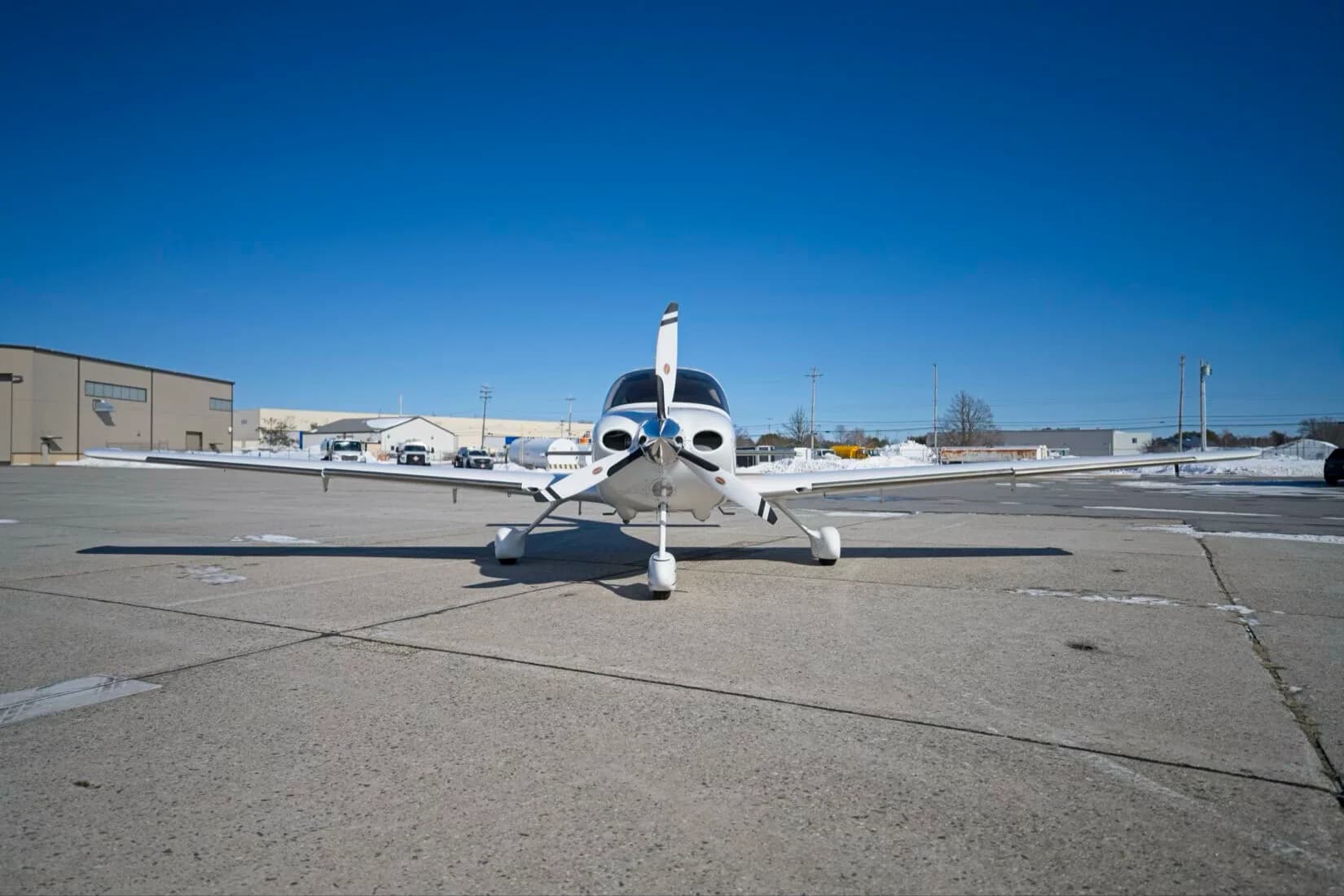 A head-on view of a white Cirrus SR22 aircraft with its propeller vertical, parked on a tarmac.