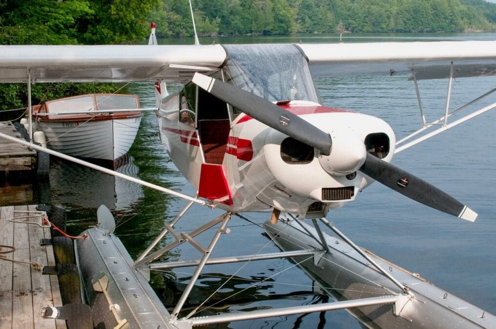 A white and red float plane is docked on a lake.