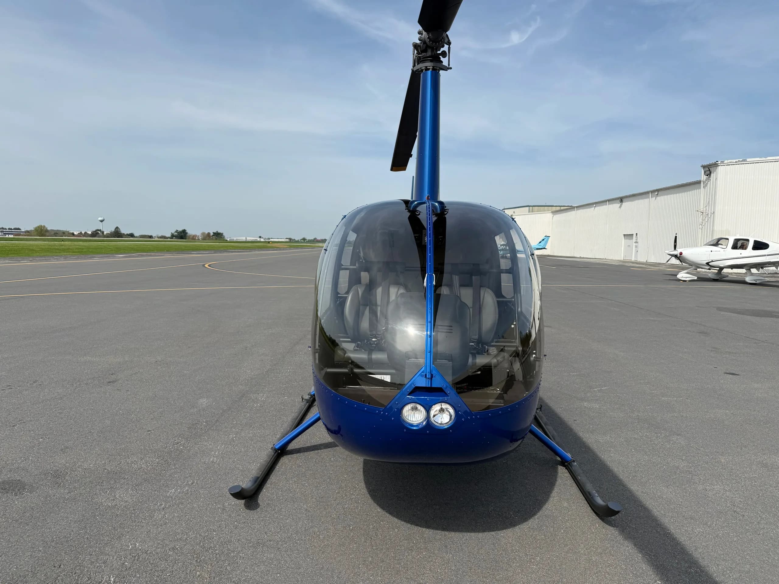 A head-on view of a blue Robinson R44 helicopter parked on an asphalt tarmac.