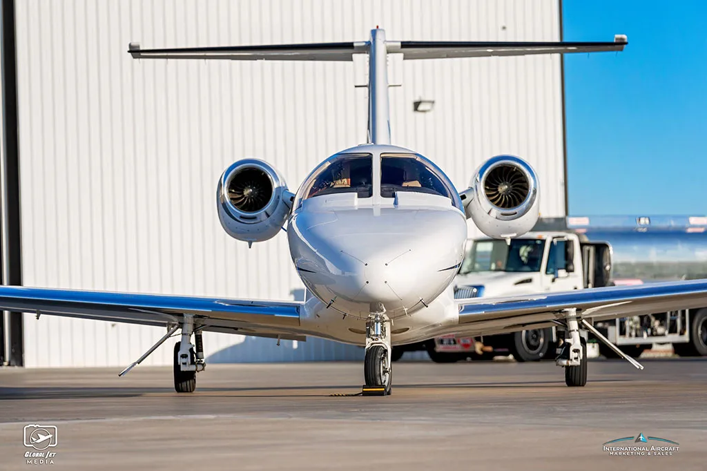 A head-on view of a white Cessna Citation CJ3 (N903GW) parked on an airfield with a fuel truck behind it.