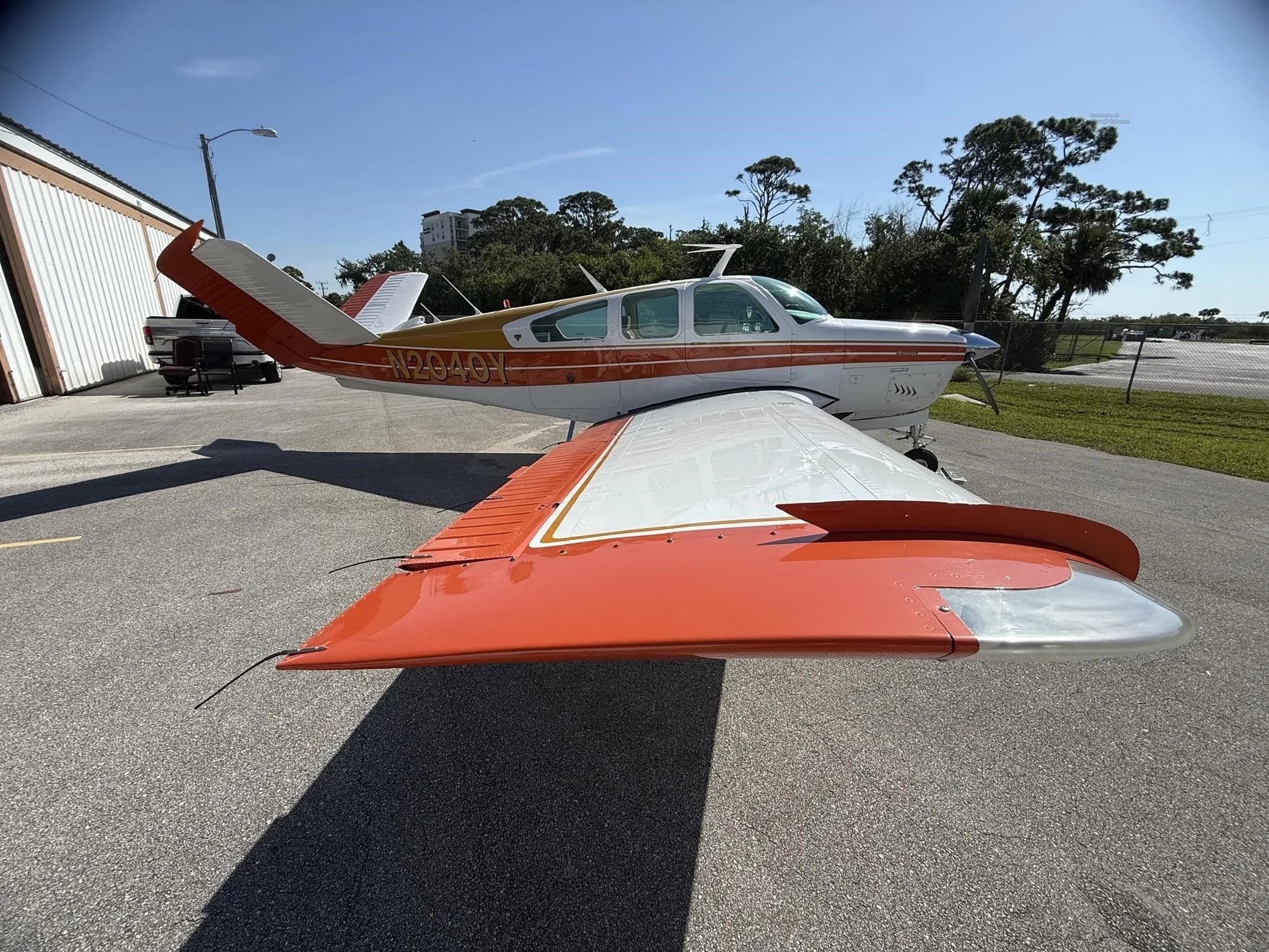 The left wing and tail of a white and orange single-engine aircraft, N2040Y, parked on an asphalt ramp.