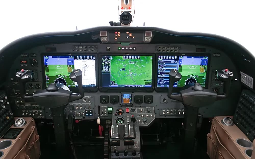 The cockpit of a modern business jet, featuring multiple large digital displays showing navigation and flight information.