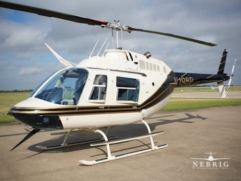 A white and black Bell 206B JetRanger III helicopter with gold trim, registration N196P, parked on an airfield.