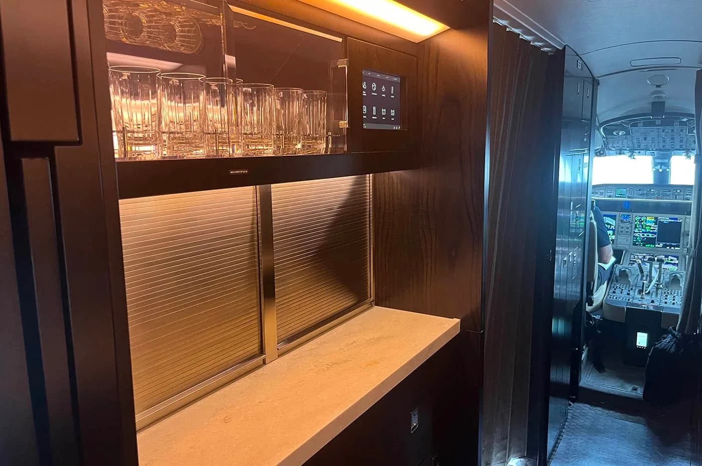 The aircraft galley area with glassware on a shelf, looking forward towards the cockpit.