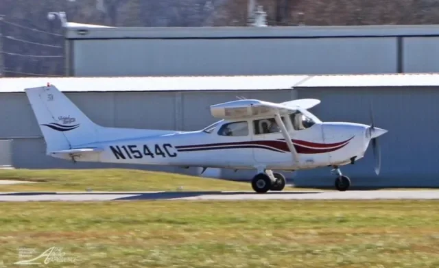 A white Cessna N1544C with red stripes taxiing on a runway, seen from the side.