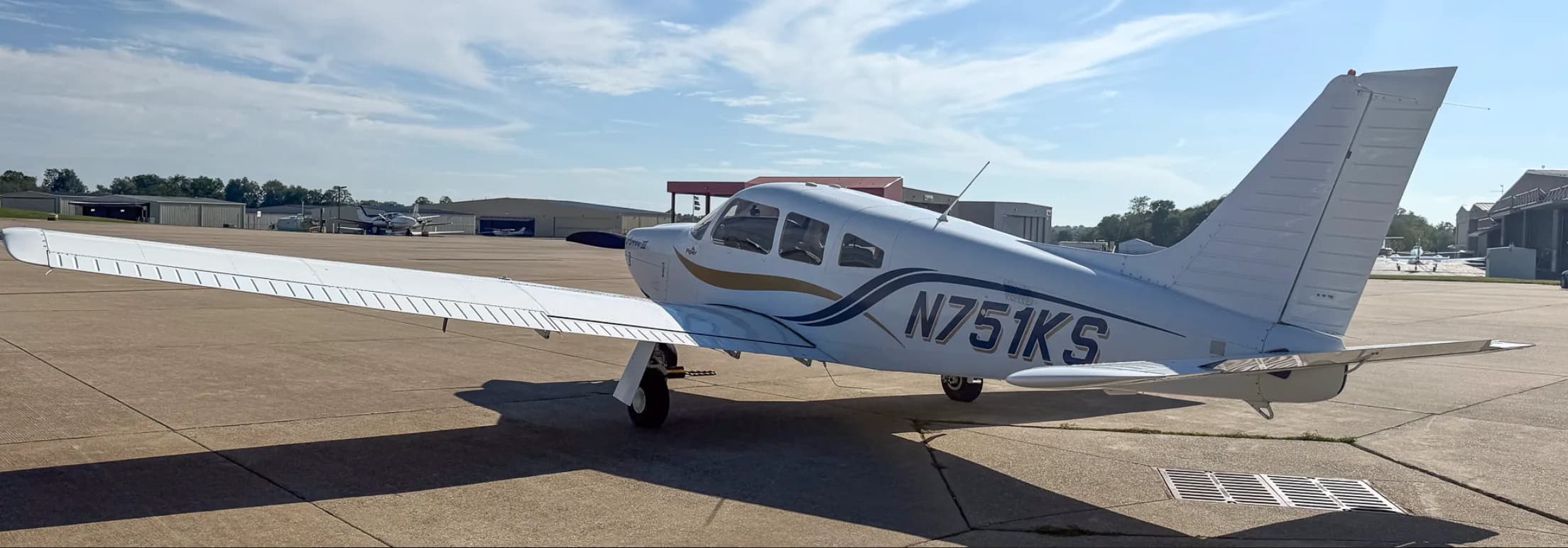 A three-quarter rear view of the white Piper Arrow III aircraft, tail number N751KS, parked on an airport tarmac.