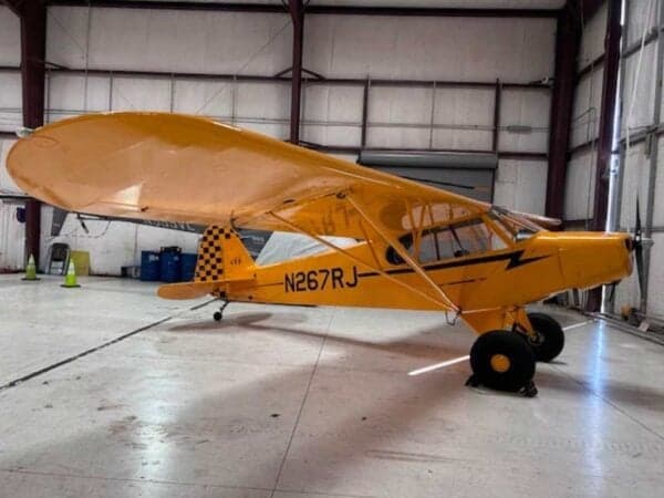 Side view of a yellow Legend Cub aircraft with registration N267RJ, parked inside a hangar.