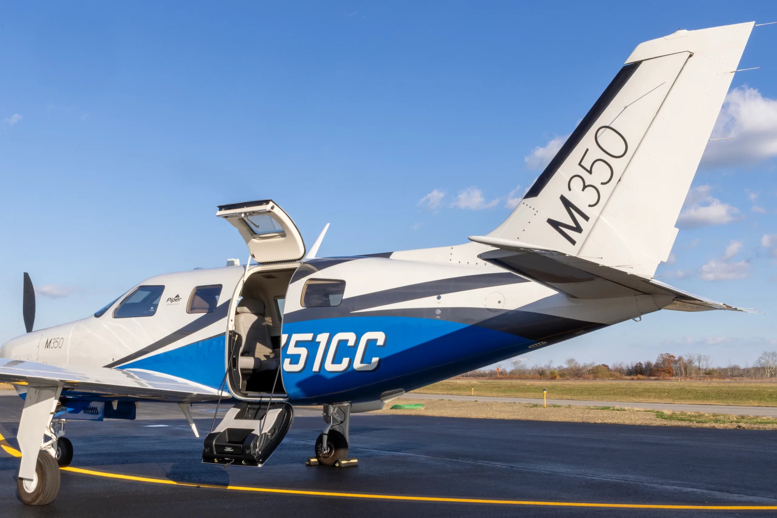 A Piper M350 aircraft, registration N751CC, with its passenger door open, parked on an airfield.