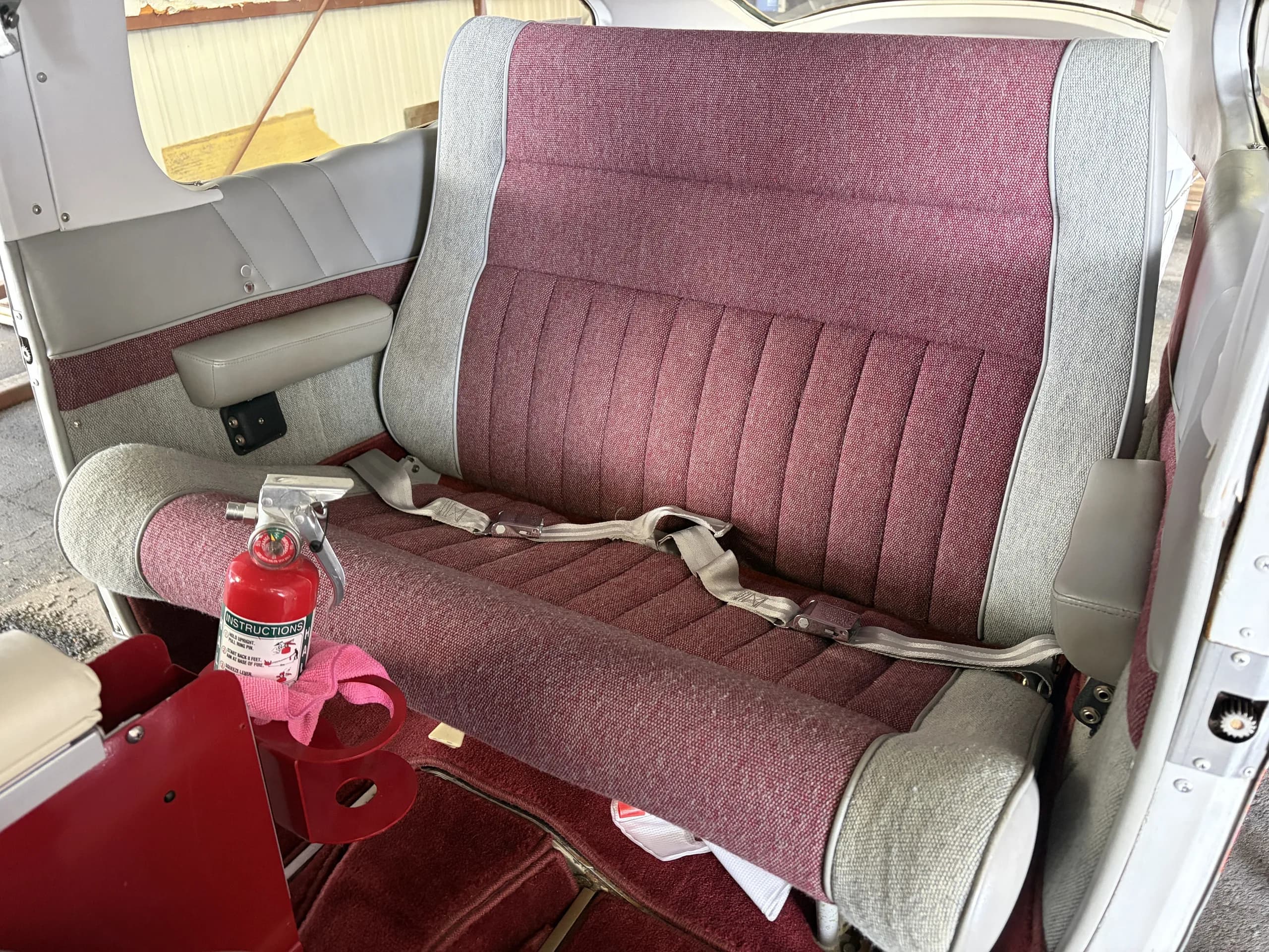 The rear seats of the aircraft, upholstered in red and grey fabric, with a fire extinguisher on the floor.