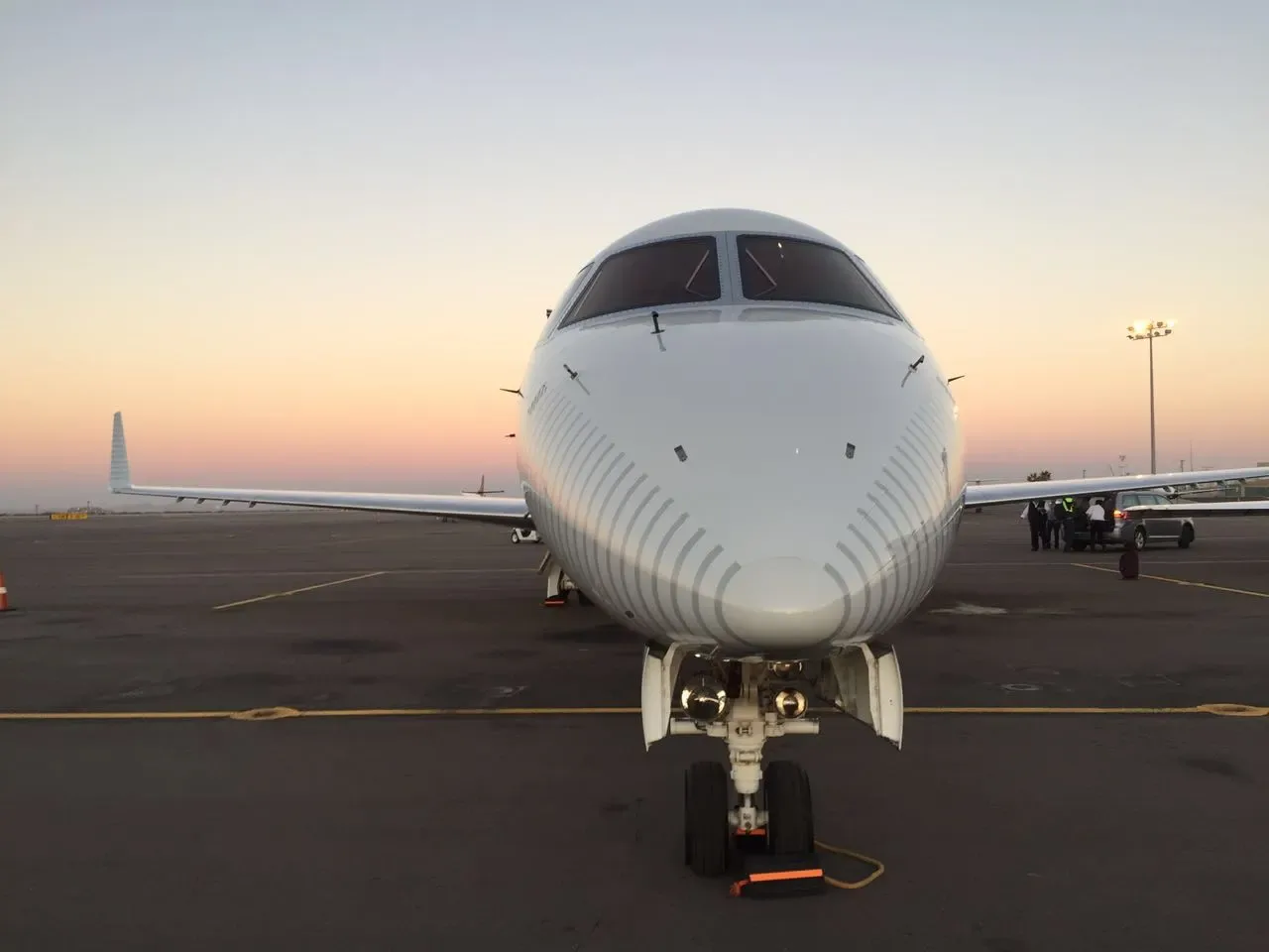 A head-on view of a white Embraer Legacy 600 business jet on the tarmac at sunset.