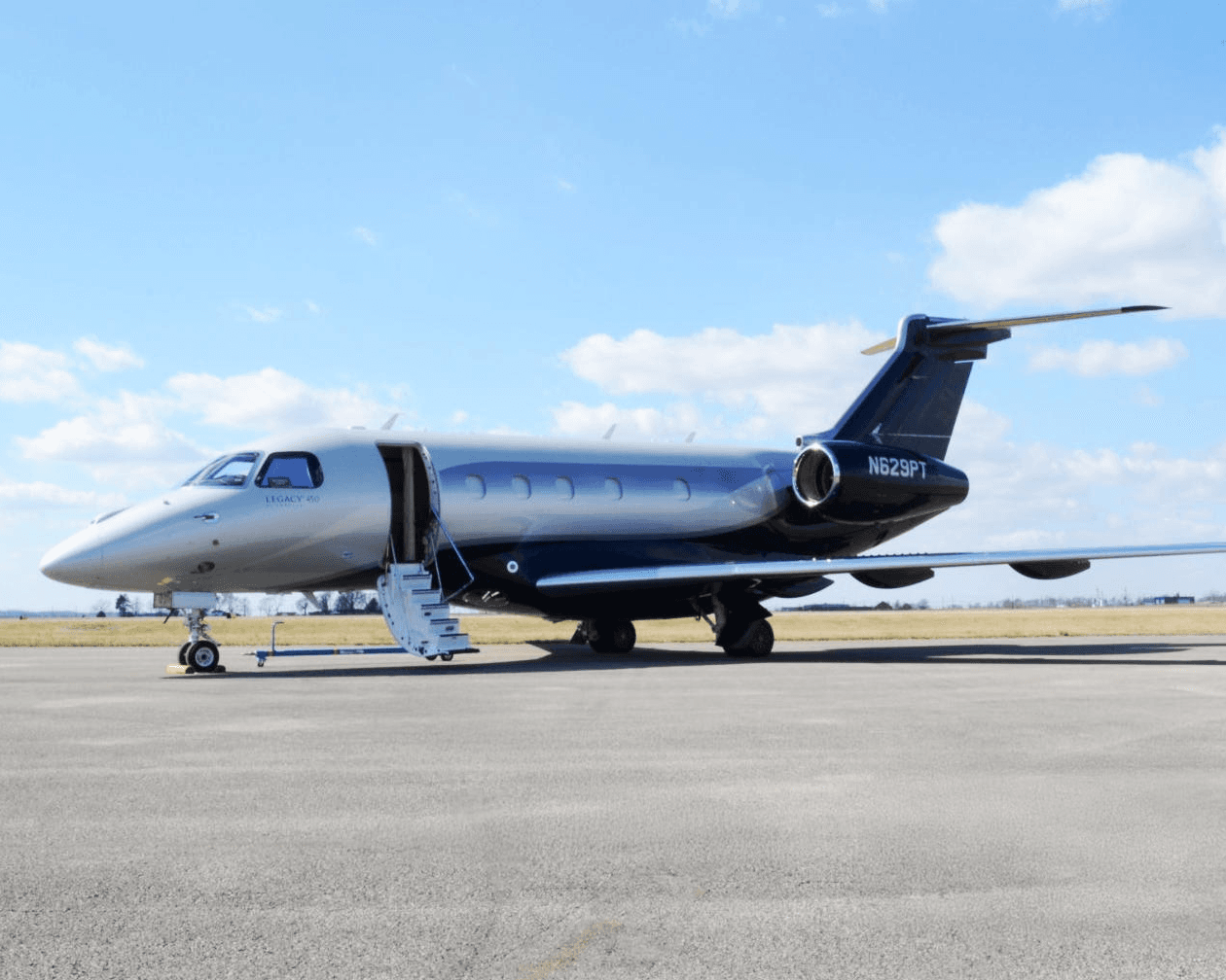 A silver and dark blue Embraer Legacy 600 private jet, tail number N629PT, parked on an airfield with its main door open and stairs extended.