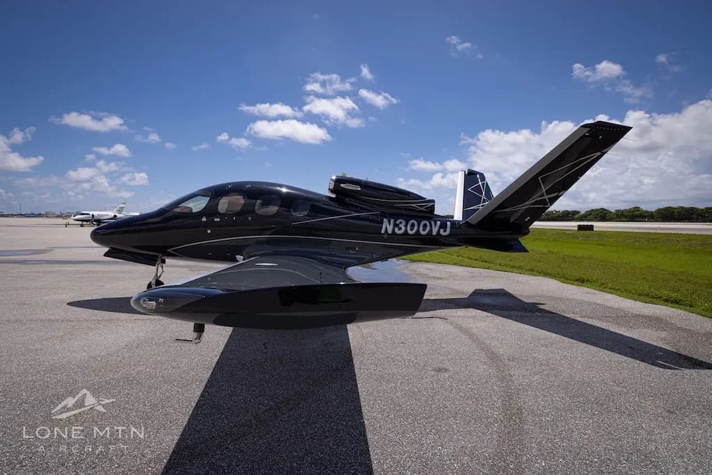 A black Cirrus Vision Jet (N300VJ) with silver accents parked on an airport tarmac, viewed from the front-right at a low angle.