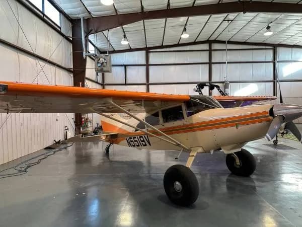 A Maule aircraft with registration N5519V, painted white and orange, viewed from the front right in a hangar.