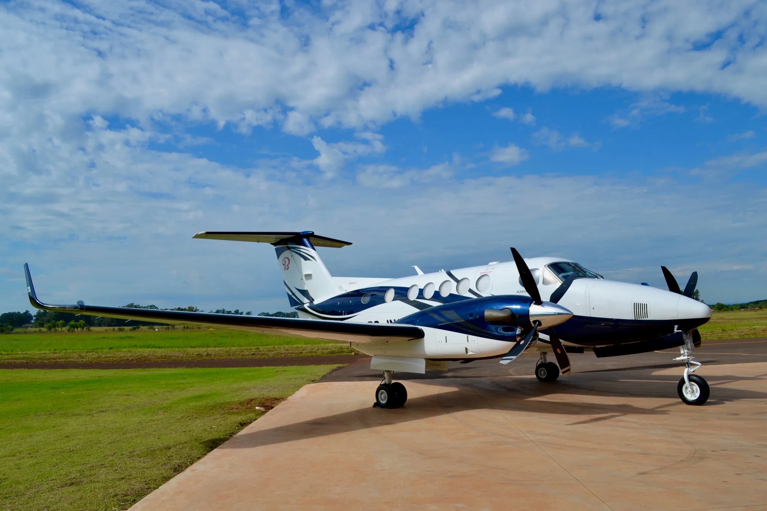 A white and blue twin-turboprop aircraft with a distinctive paint scheme parked on a tarmac under a partly cloudy sky.