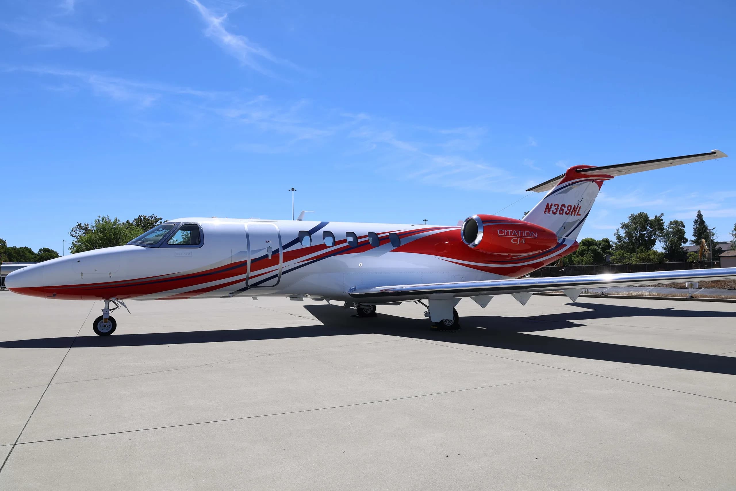 A side view of the white Cessna Citation CJ4 (N369NL) with red and blue stripes, parked on an airfield.