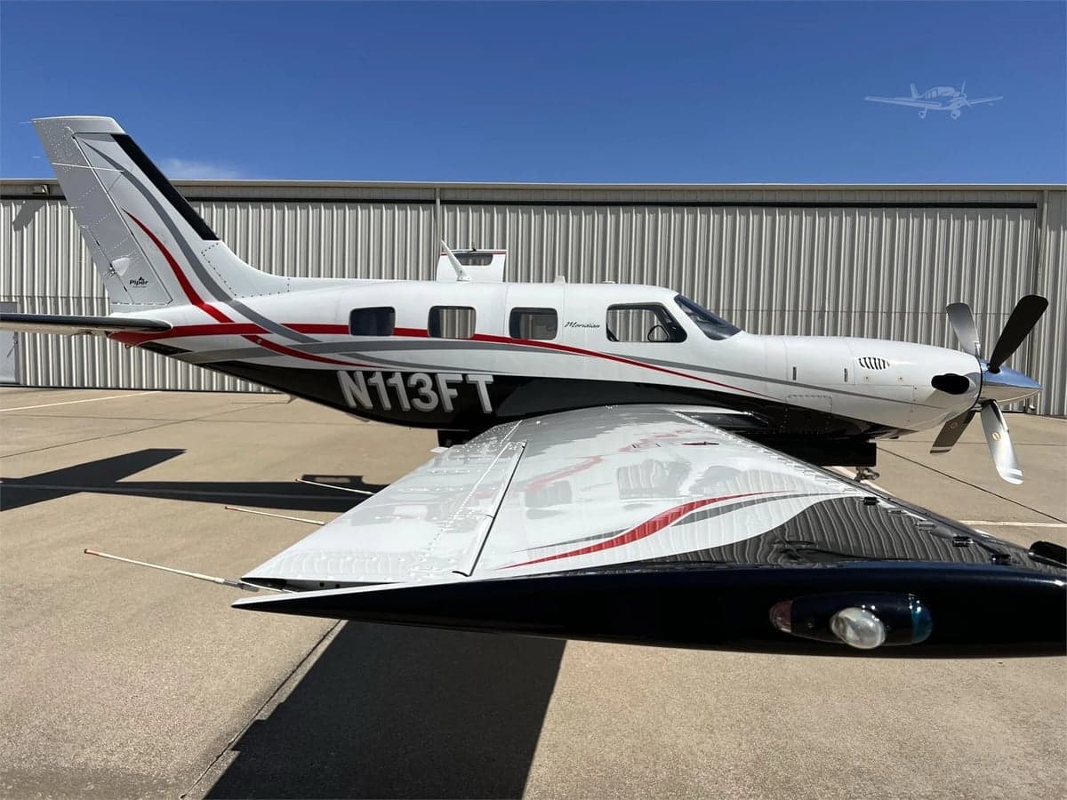 Side view of a Piper Meridian aircraft with a white, black, and red paint scheme parked on the tarmac.
