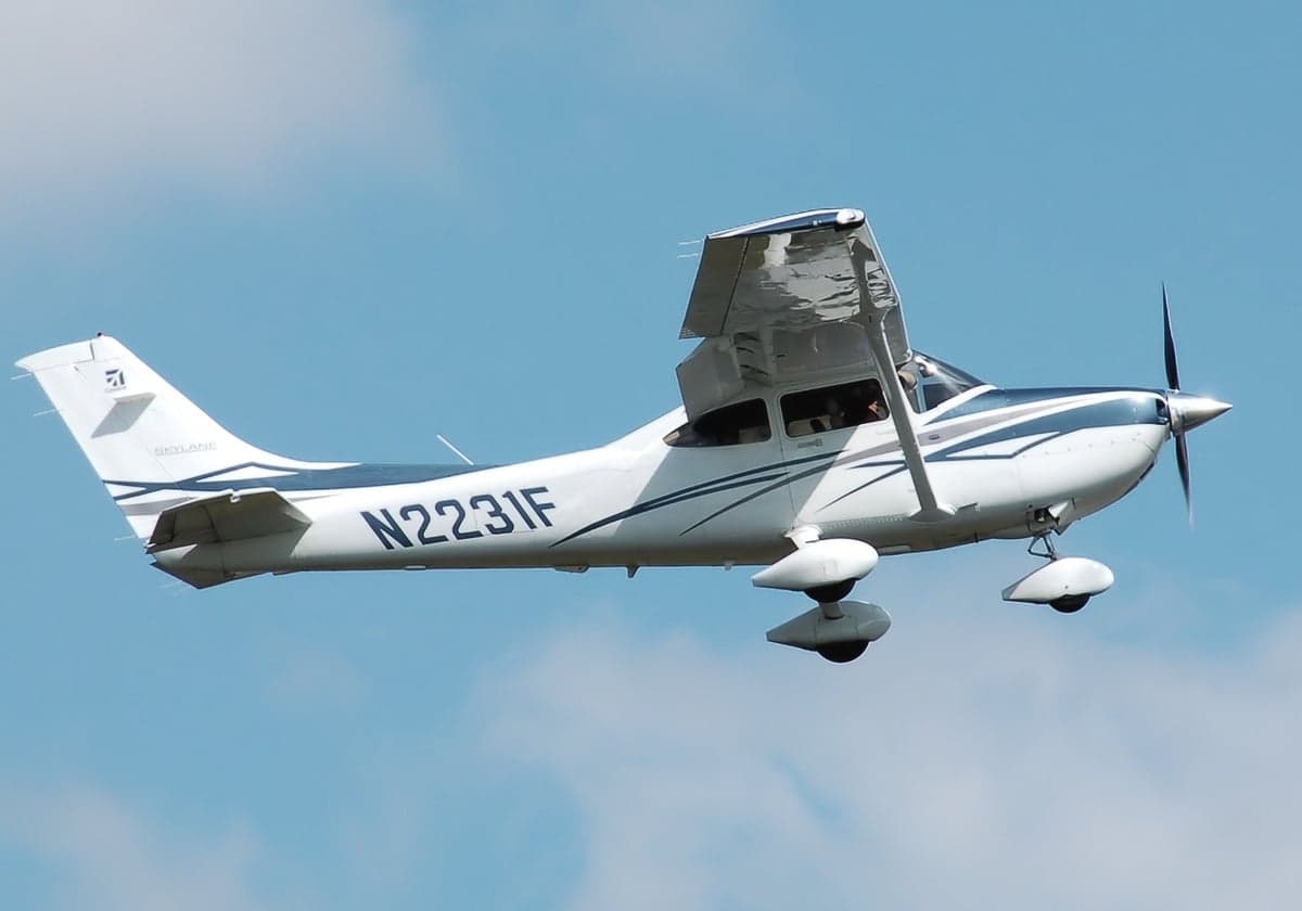 A white and blue Cessna 182 Skylane (N2231F) in flight against a blue sky.
