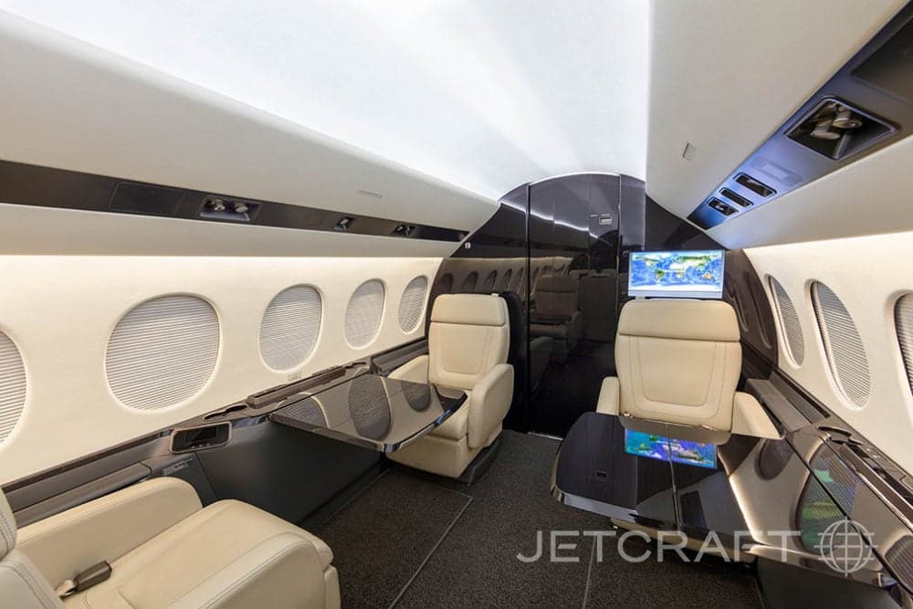 View of the aircraft interior with cream-colored seats and dark wood tables.