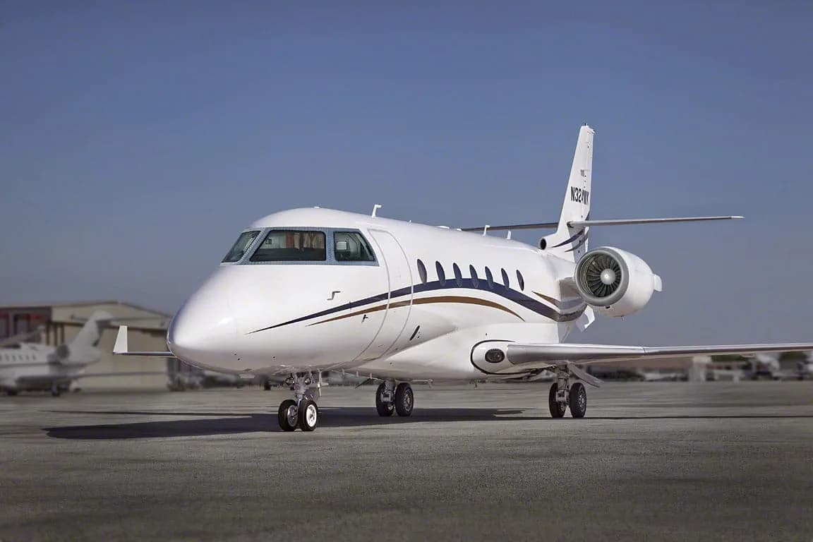 A white business jet with blue and gold stripes and tail number N324WK parked on a tarmac under a clear blue sky.