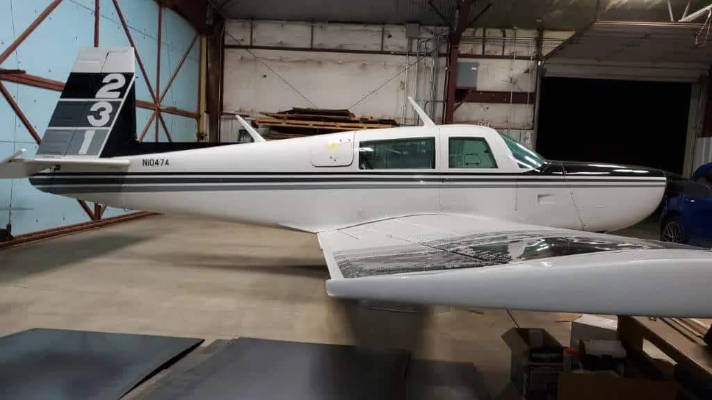 Rear-side view of a white and black Grumman American AA-5 Traveler aircraft, N1047A, inside a hangar.