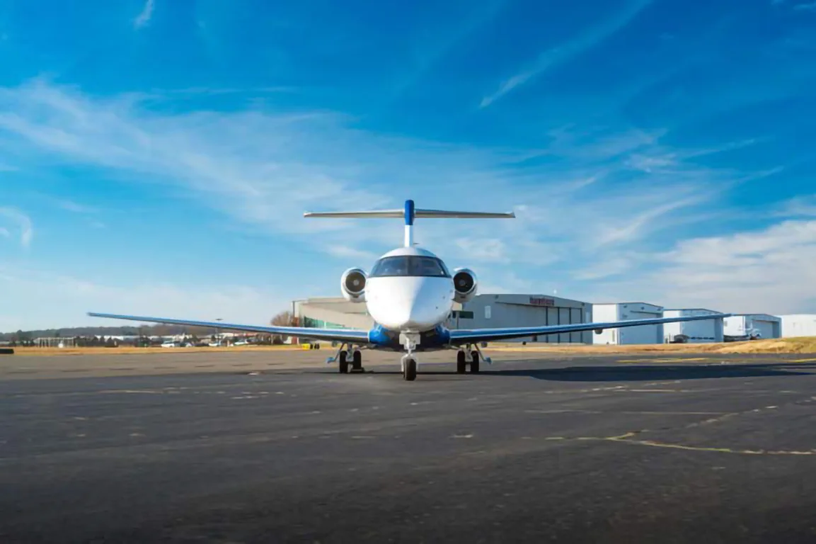A Pilatus PC-24 jet, painted white and blue, is viewed head-on while parked on an airfield.