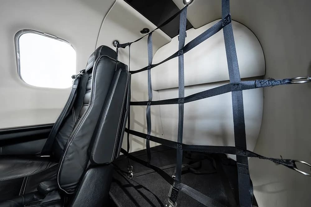 A view of the TBM 930's rear cabin area with a cargo net installed behind a black leather seat.