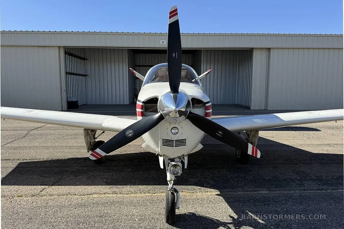 A white single-engine aircraft with a black propeller and red stripes viewed head-on on a tarmac.