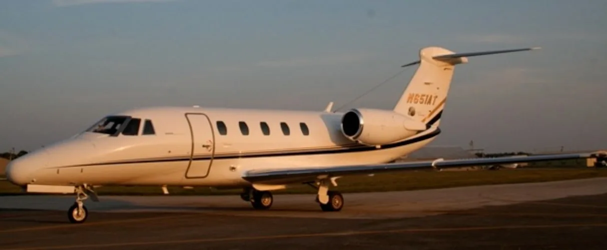 A white business jet with a dark stripe and tail number N651AT is parked on a tarmac at sunset.