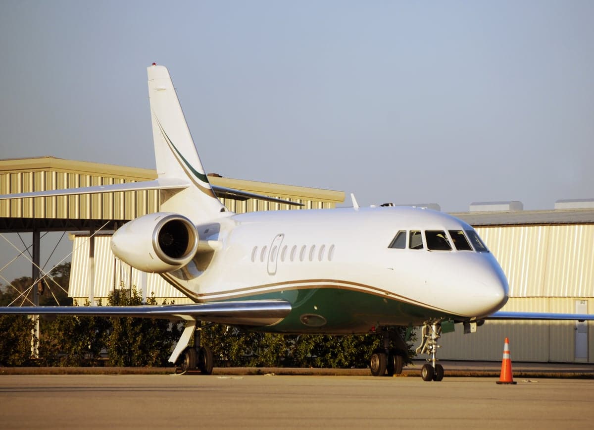 A Falcon jet parked on the tarmac with a white and green paint scheme.