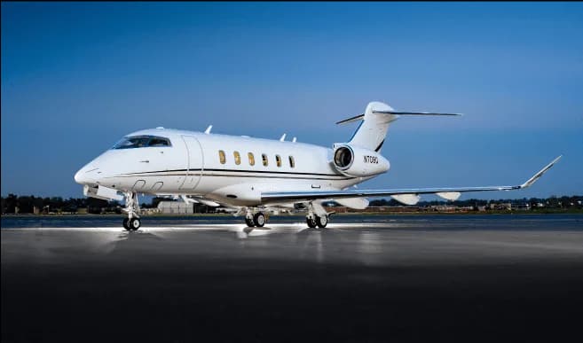 A white Bombardier Challenger 350 business jet with registration N708U is parked on an airfield at dusk.