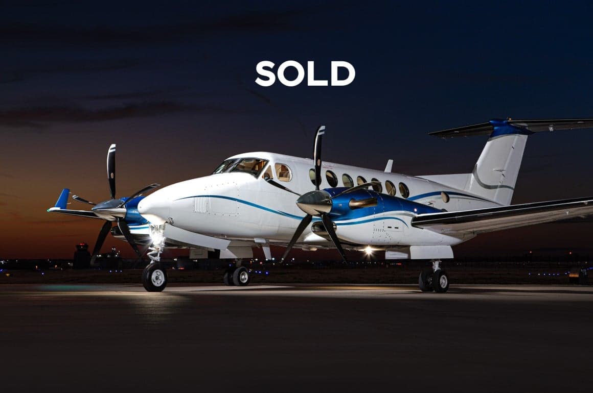 A King Air turboprop aircraft with a white and blue paint scheme is parked on the tarmac at dusk.