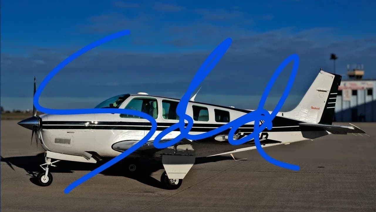 A white and black propeller aircraft, possibly a Beechcraft Baron, parked on an airfield under a clear blue sky.