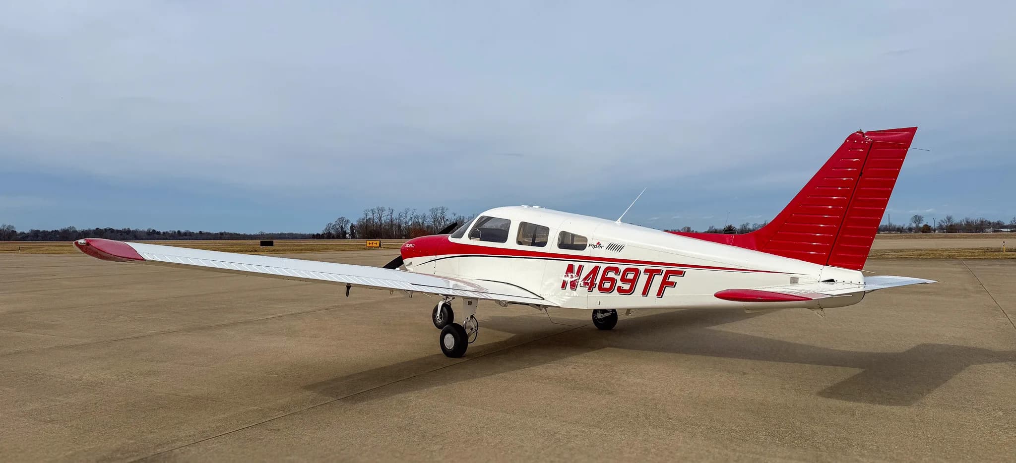 A three-quarter rear view of a white and red Piper Archer TX aircraft, N469TF, on an airfield.
