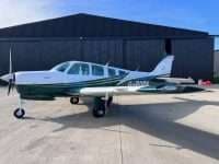 A Beechcraft Bonanza with a white and green paint scheme is parked on the tarmac.