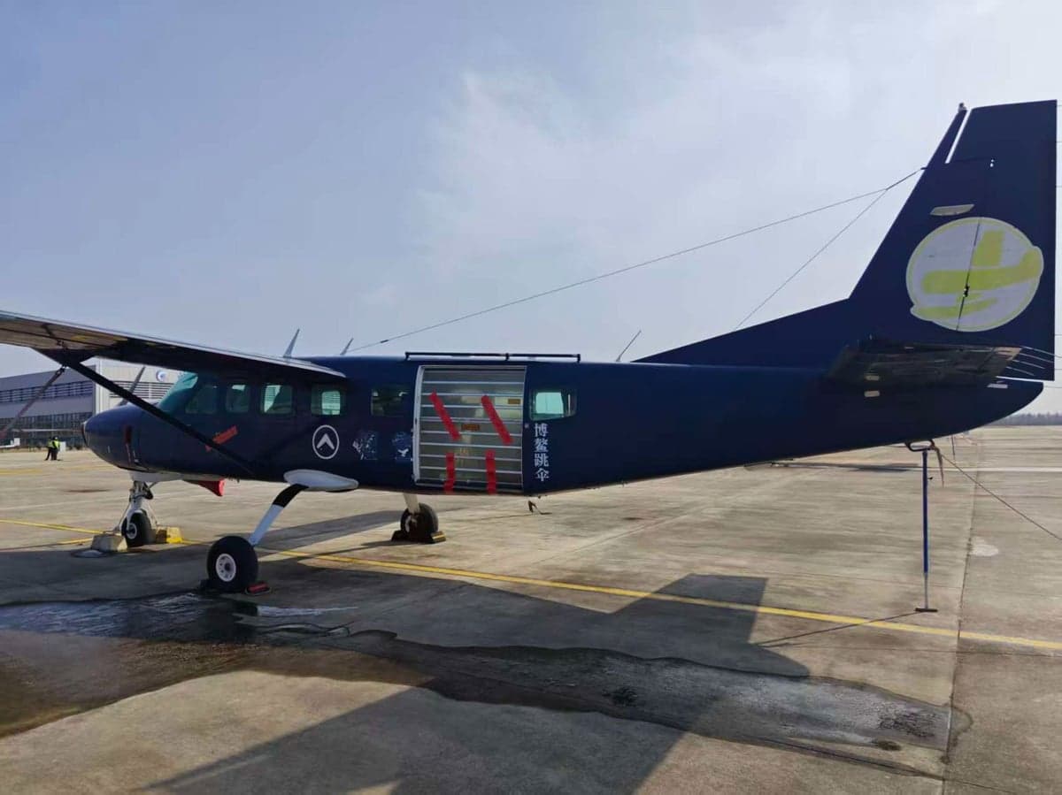 A blue aircraft is parked on the tarmac with the door open.