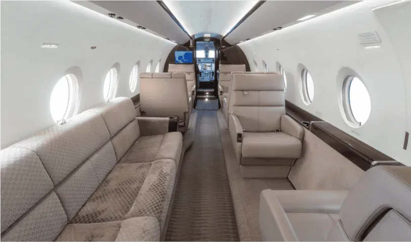 A wider view of the aircraft's luxurious cabin interior featuring a long sofa and individual light grey seats.
