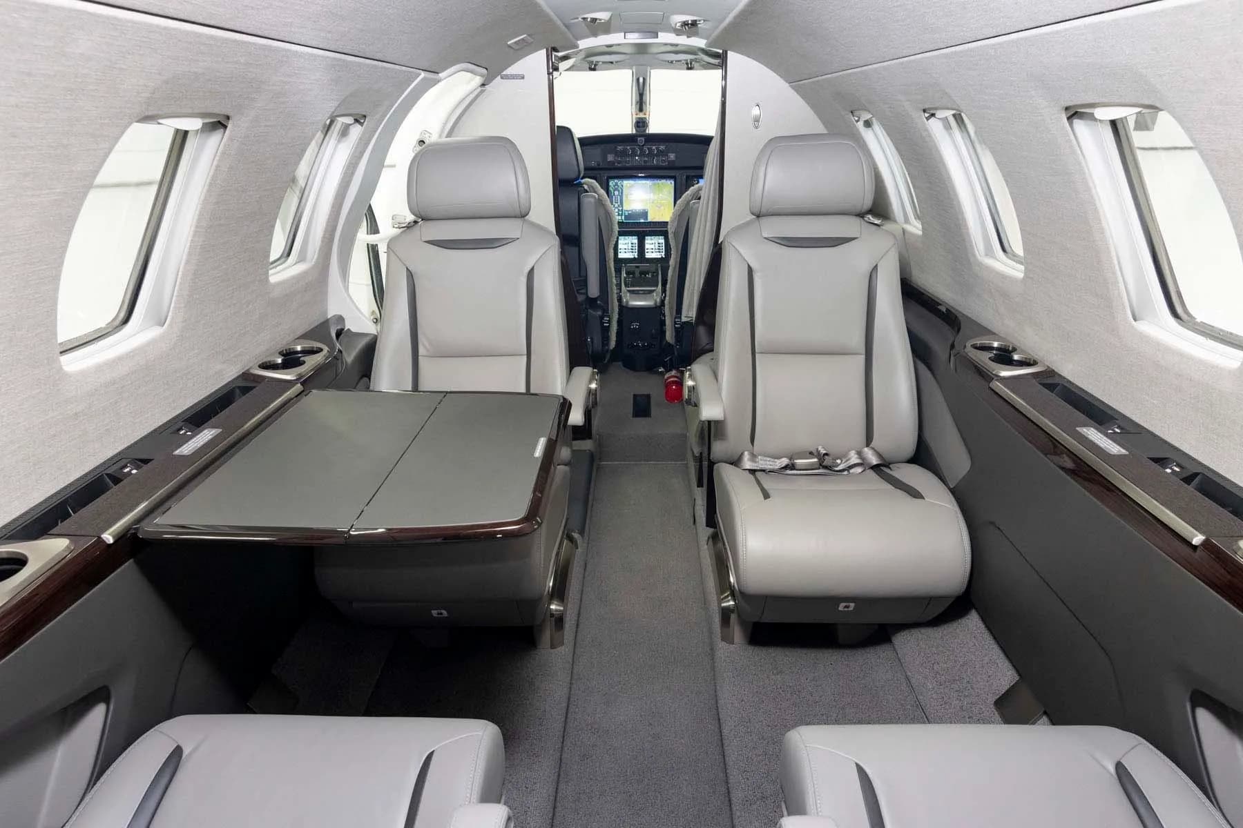 The private jet's cabin interior, looking forward towards the cockpit, with grey leather seats and a deployed table.