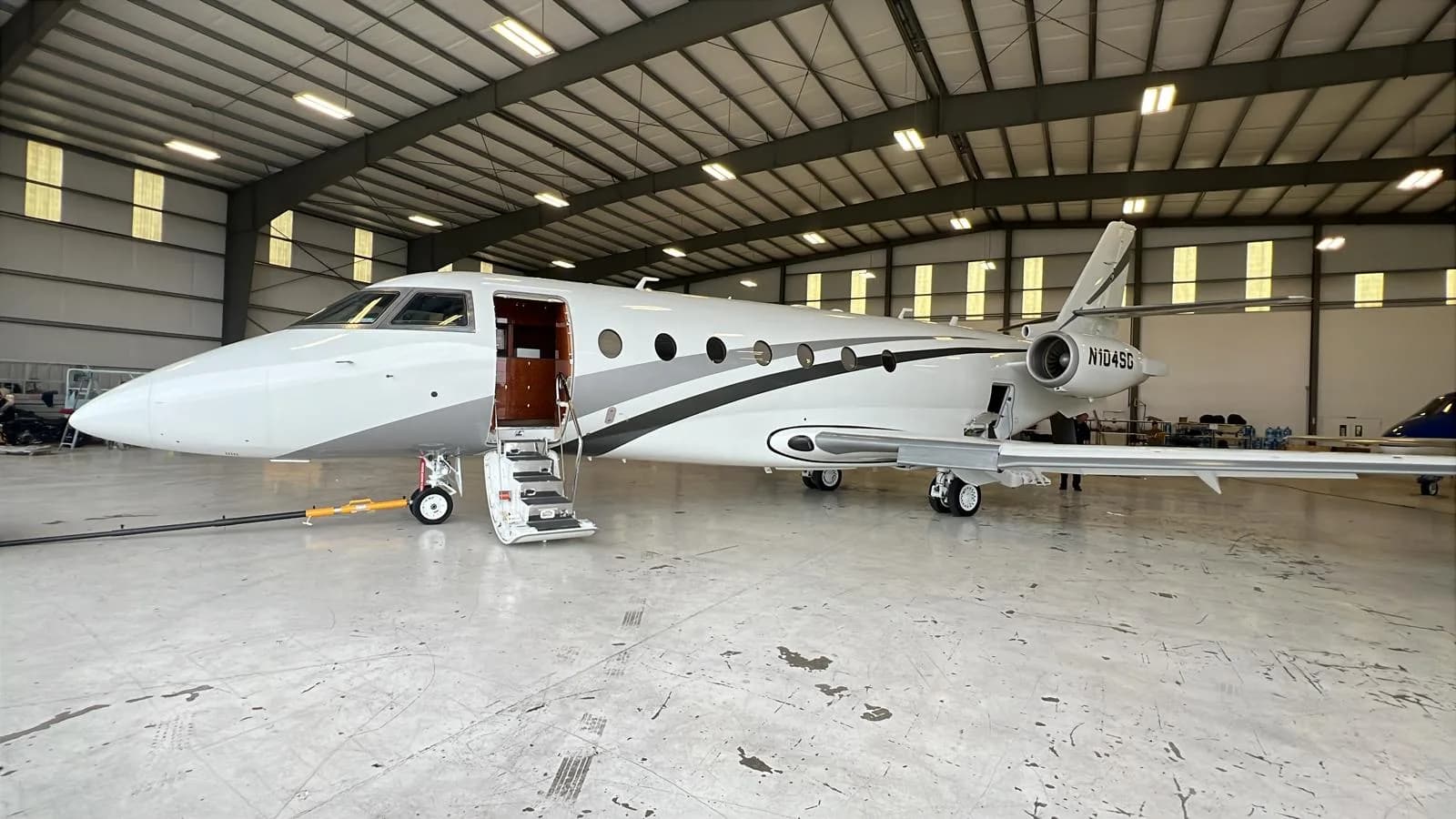 A white and gray jet with tail number N104SG sits inside a hangar with the door open.