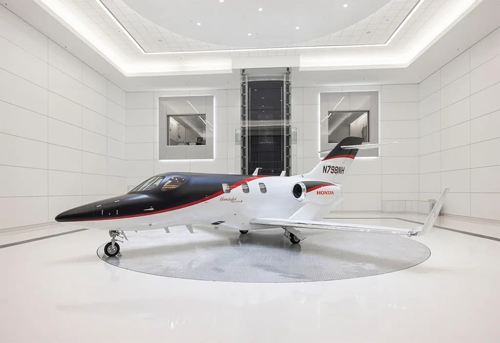 A black and white HondaJet Elite II (N798NH) with red accents is displayed on a rotating platform in a modern white showroom.