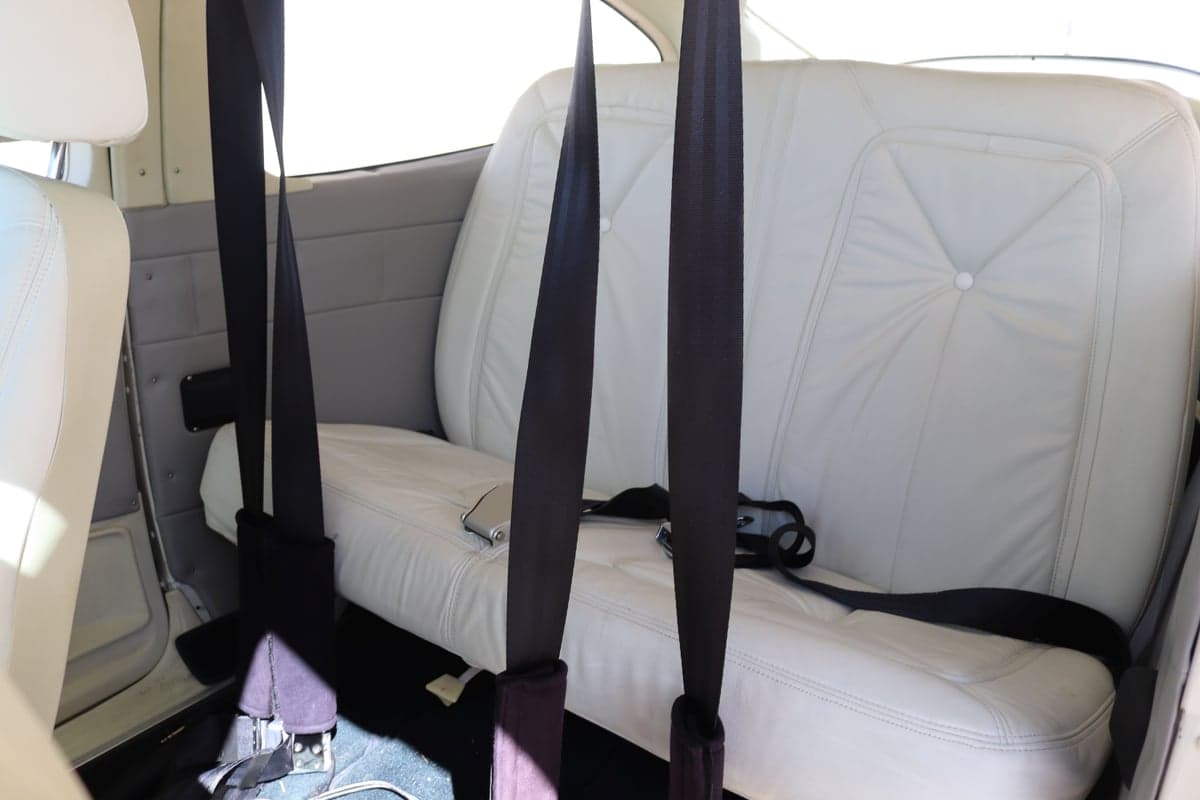 Rear cabin seats with white upholstery and black seatbelts.