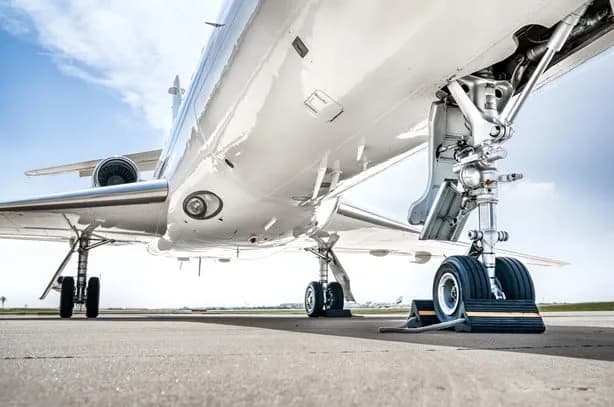 A low-angle view of the main landing gear and underside of a white business jet on an airport tarmac.